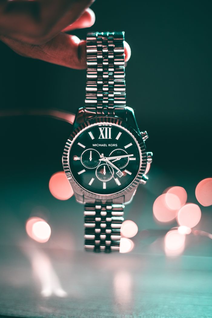 services-01 Silver Michael Kors wristwatch with Roman numerals and elegant design, highlighted by bokeh lights.